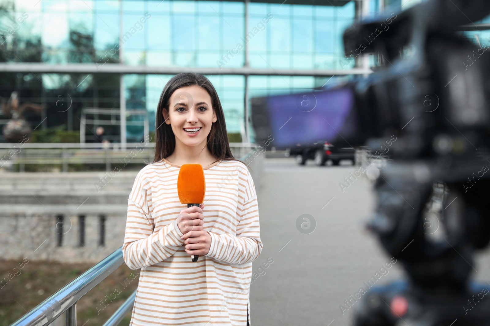 Photo of Young female journalist with microphone working on city street