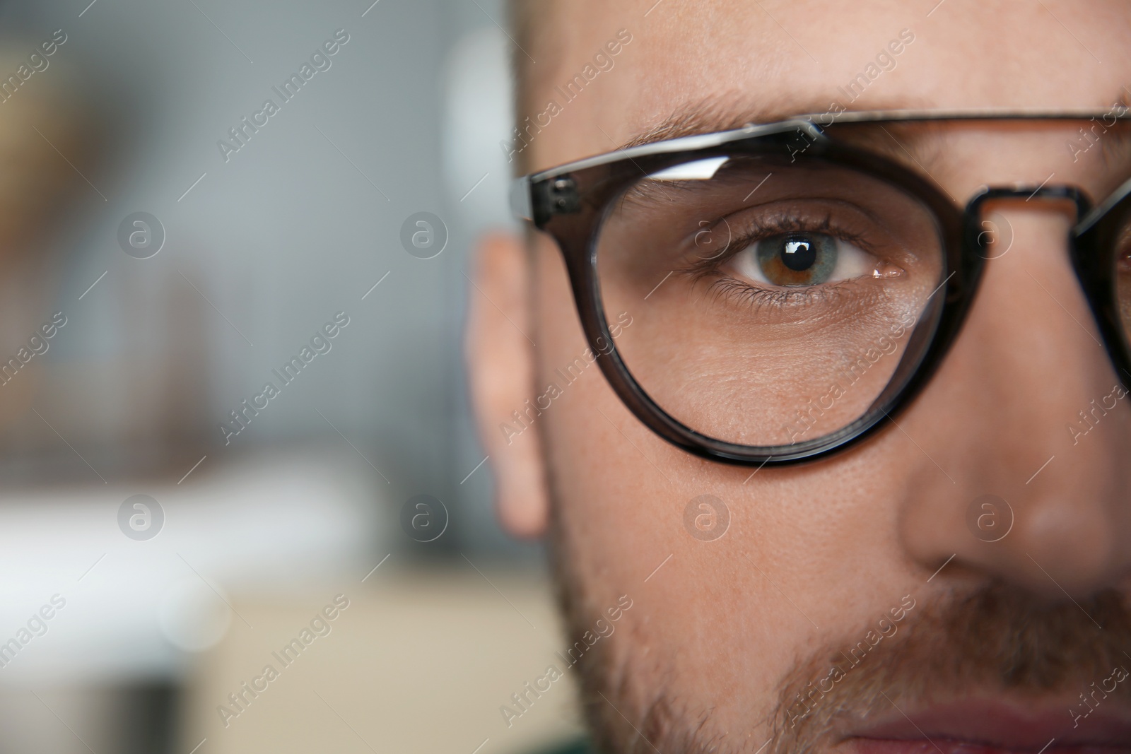 Photo of Young man wearing glasses on blurred background, closeup. Ophthalmology service