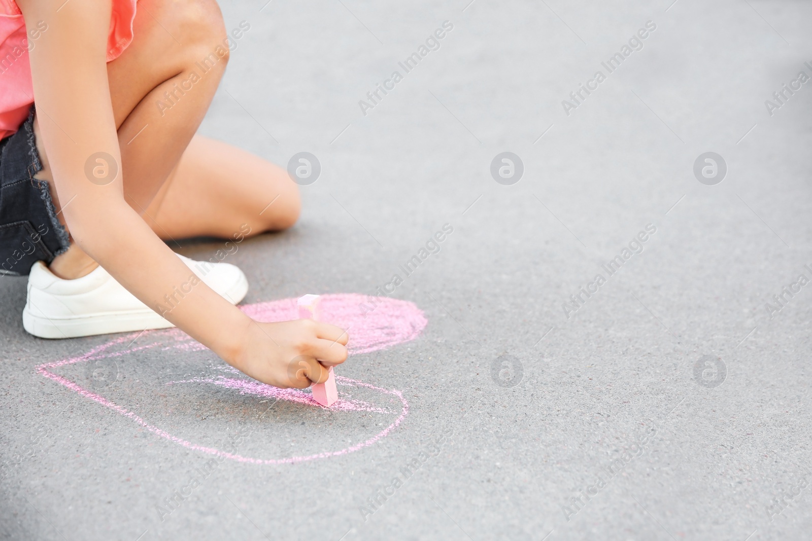 Photo of Little child drawing heart with chalk on asphalt, closeup