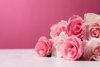 Photo of Beautiful roses on light table against pink background, closeup. Space for text