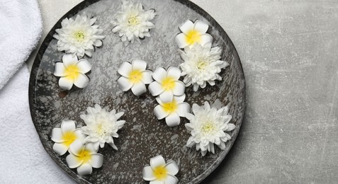 Bowl of water with flowers on light grey table, top view and space for text. Spa treatment