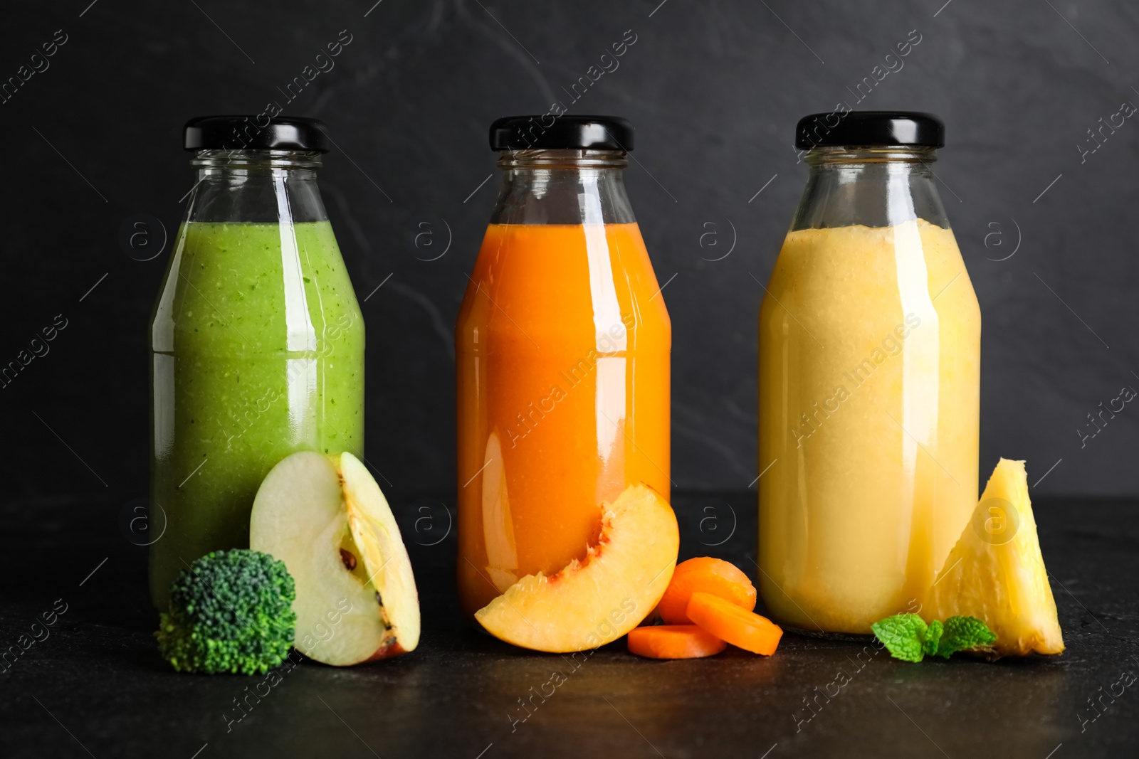 Photo of Bottles with delicious colorful juices and fresh ingredients on black table