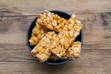 Photo of Delicious peanut kozinaki bars in bowl on wooden table, top view