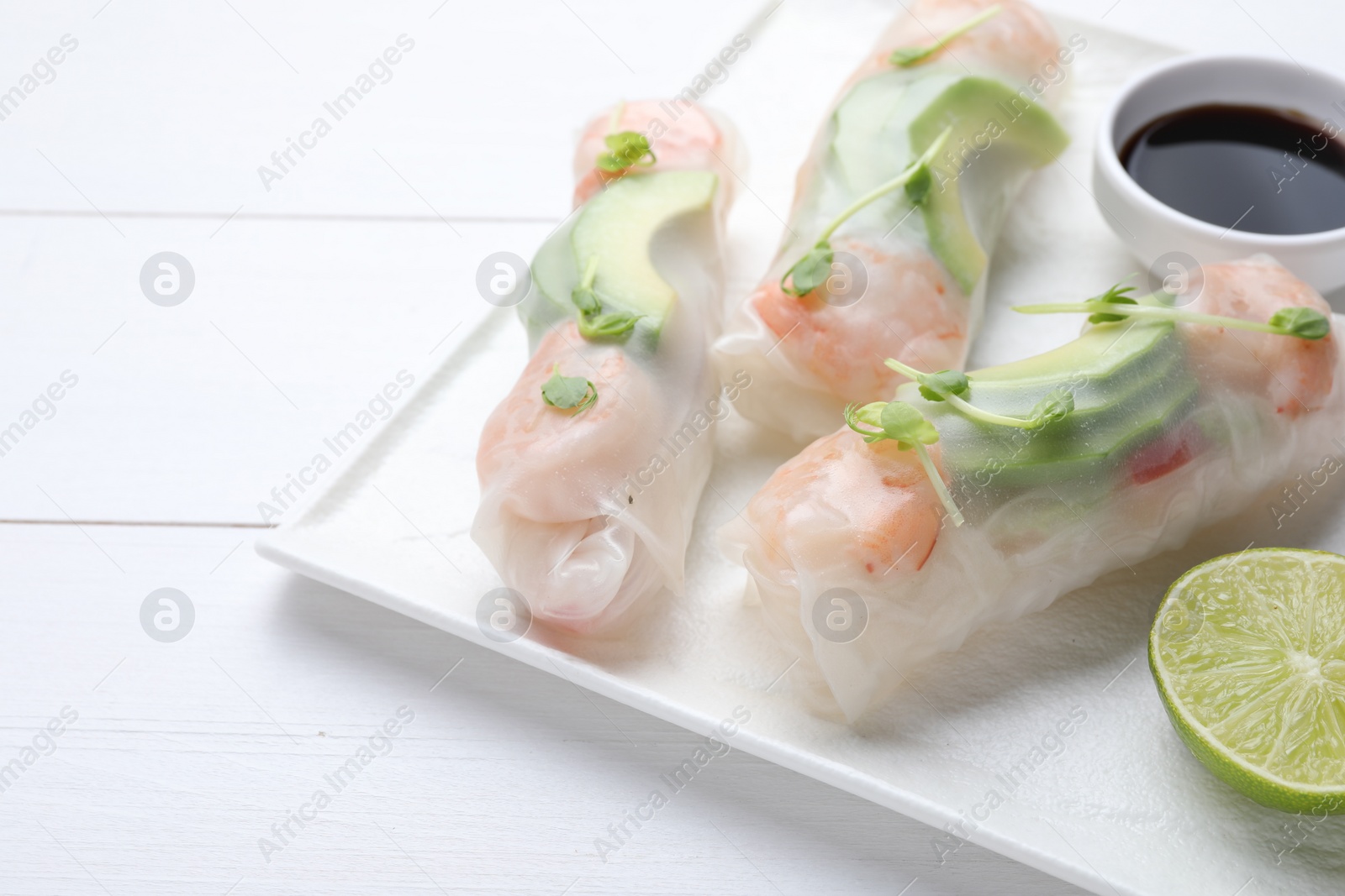 Photo of Delicious spring rolls, lime and soy sauce on white wooden table, closeup