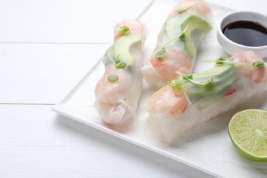 Delicious spring rolls, lime and soy sauce on white wooden table, closeup