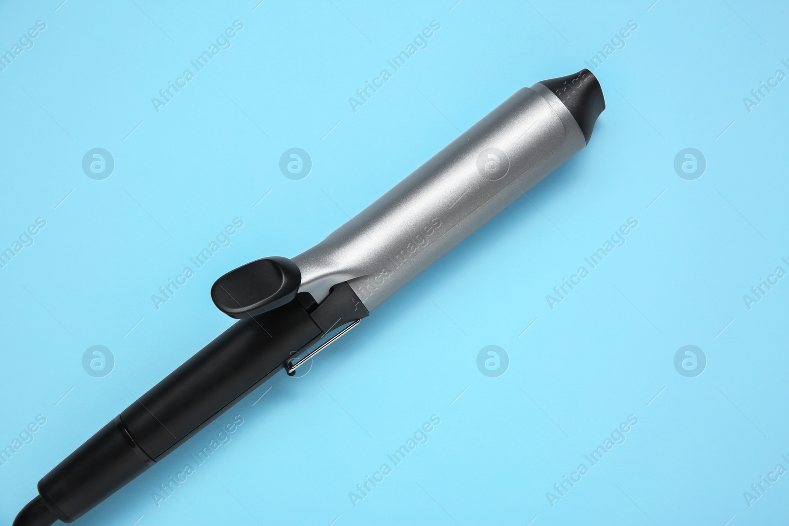Photo of Hair styling appliance. One curling iron on light blue background, top view