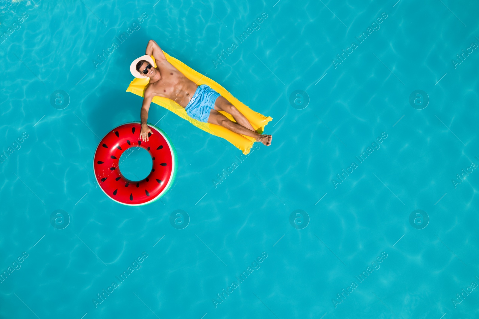 Image of Happy man with inflatable mattress and ring in swimming pool, top view. Summer vacation