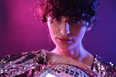 Photo of Beautiful young woman with disco ball posing on color background in neon lights, closeup