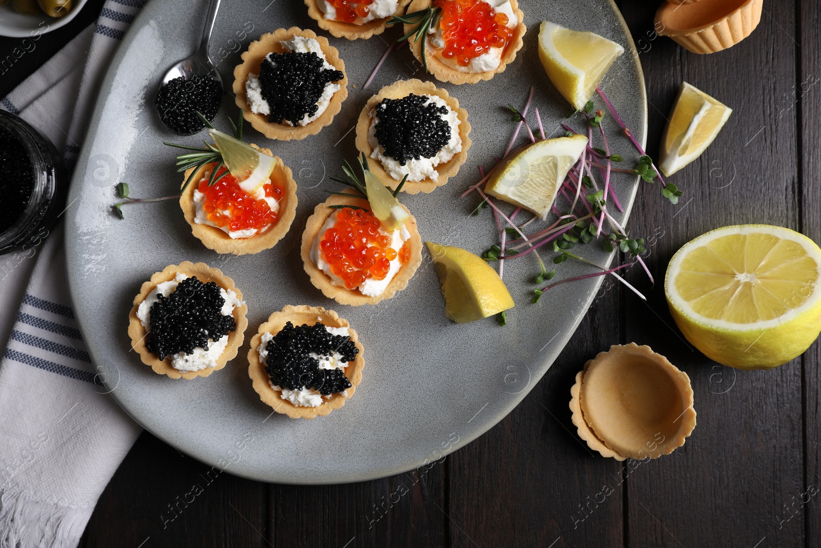 Photo of Delicious tartlets with red and black caviar served on wooden table, flat lay