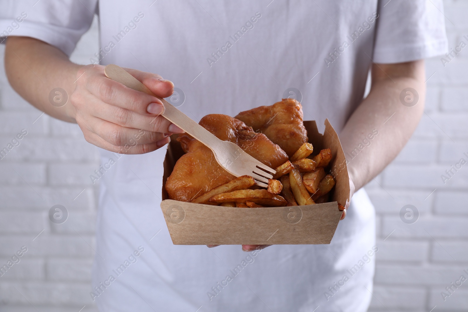 Photo of Woman eating fish and chips near white brick wall, closeup