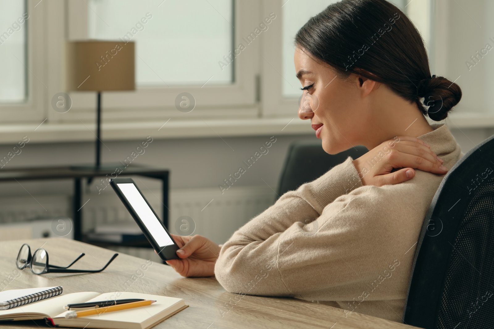 Photo of Young woman using e-book reader at wooden table indoors