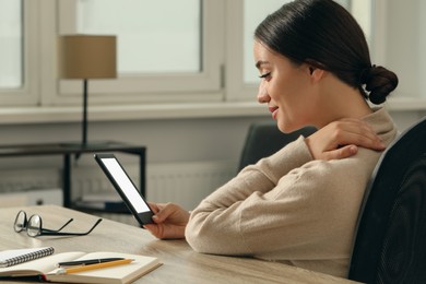 Young woman using e-book reader at wooden table indoors