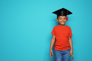 Little African-American school child with graduate cap on color background