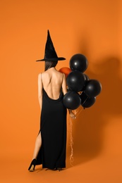 Photo of Young woman wearing witch costume with balloons for Halloween party on yellow background