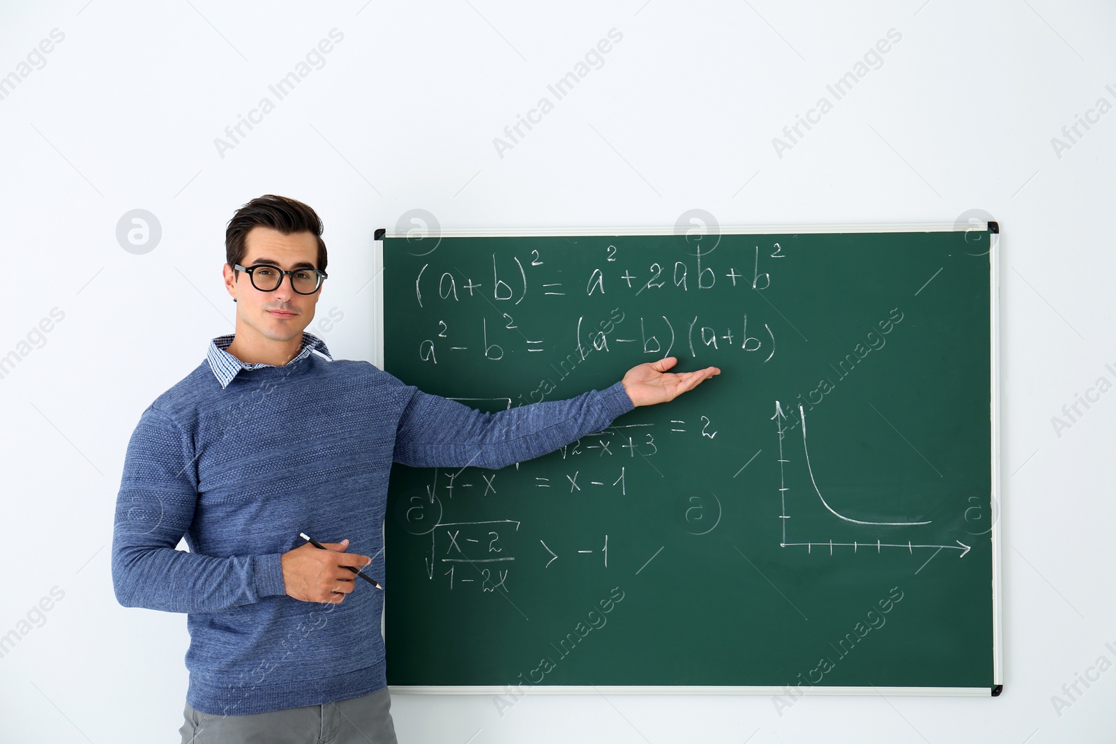 Photo of Young teacher explaining math formulas written on chalkboard in classroom