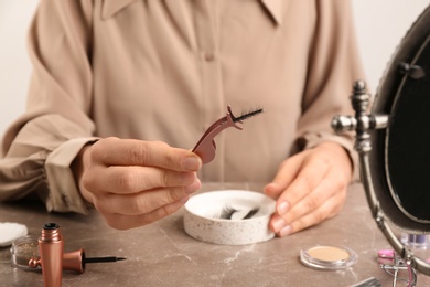 Photo of Woman holding tweezers with magnetic eyelashes at grey table, closeup