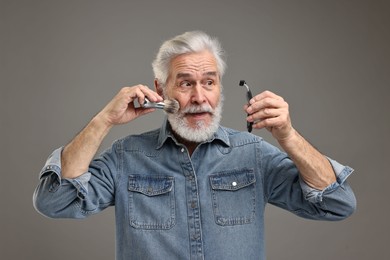 Photo of Senior man with mustache holding razor and brush on grey background