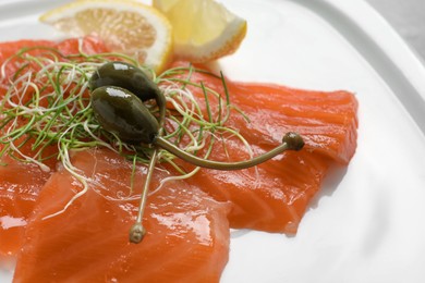 Photo of Salmon carpaccio with capers, microgreens and lemon on plate, closeup