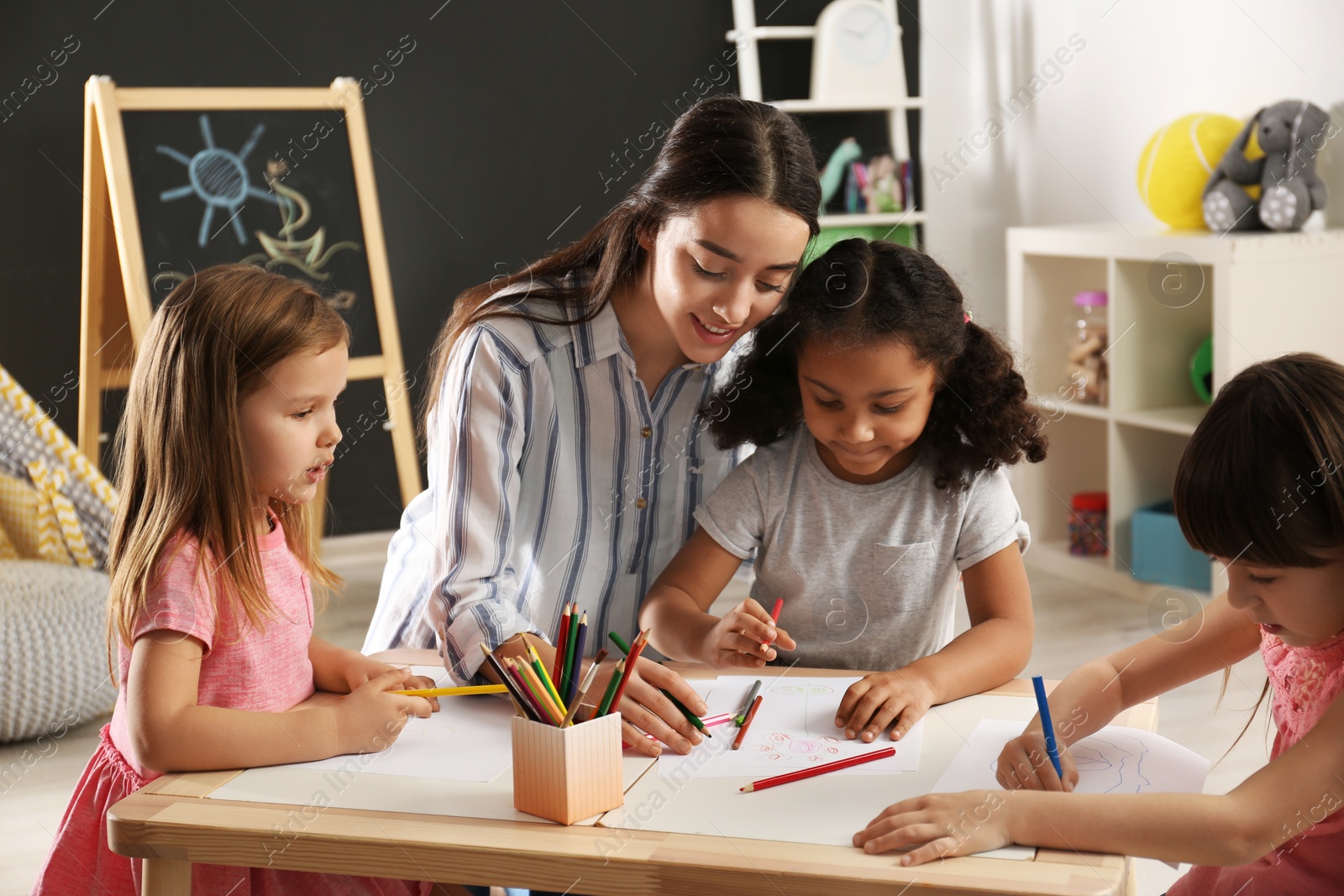 Photo of Cute little children with nursery teacher drawing at table in kindergarten. Indoor activity