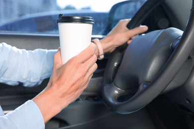 Coffee to go. Woman with paper cup of drink driving her car, closeup