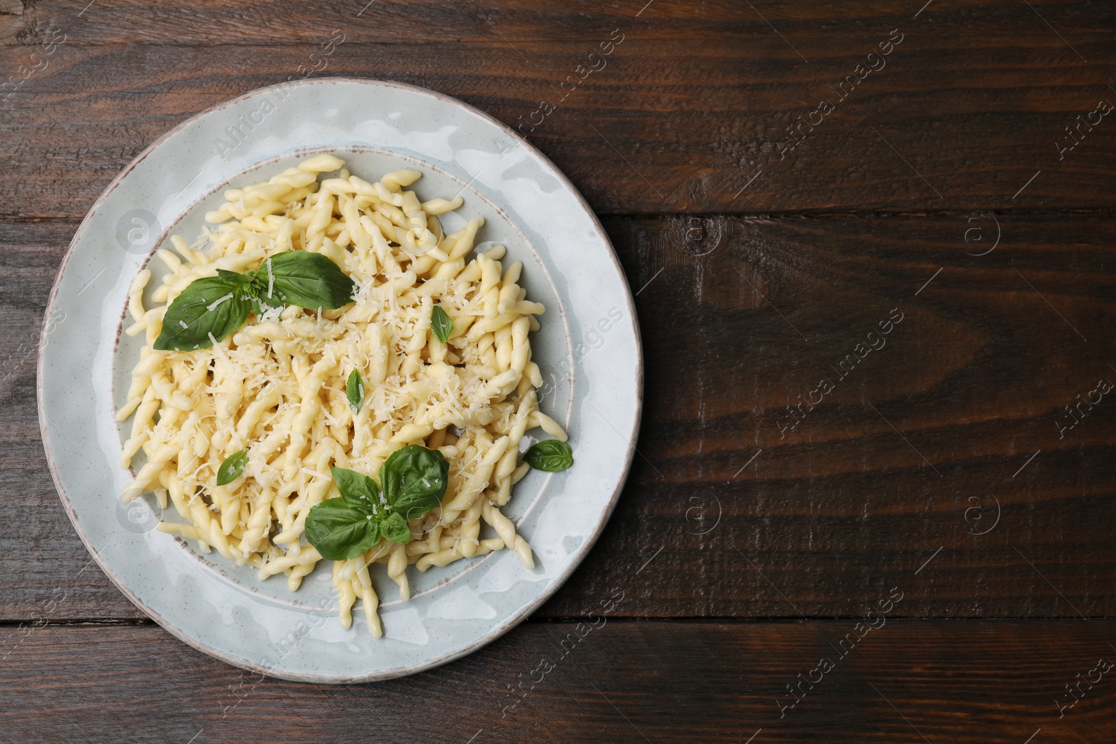 Photo of Plate of delicious trofie pasta with cheese and basil leaves on wooden table, top view. Space for text