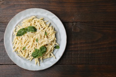 Plate of delicious trofie pasta with cheese and basil leaves on wooden table, top view. Space for text