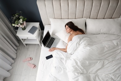 Photo of Tired woman with laptop and smartphone sleeping in bed at home, above view