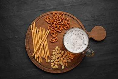 Glass of beer served with delicious pretzel crackers and other snacks on black table, top view