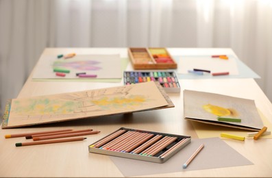 Photo of Artist's workplace with drawings, soft pastels and color pencils on table indoors