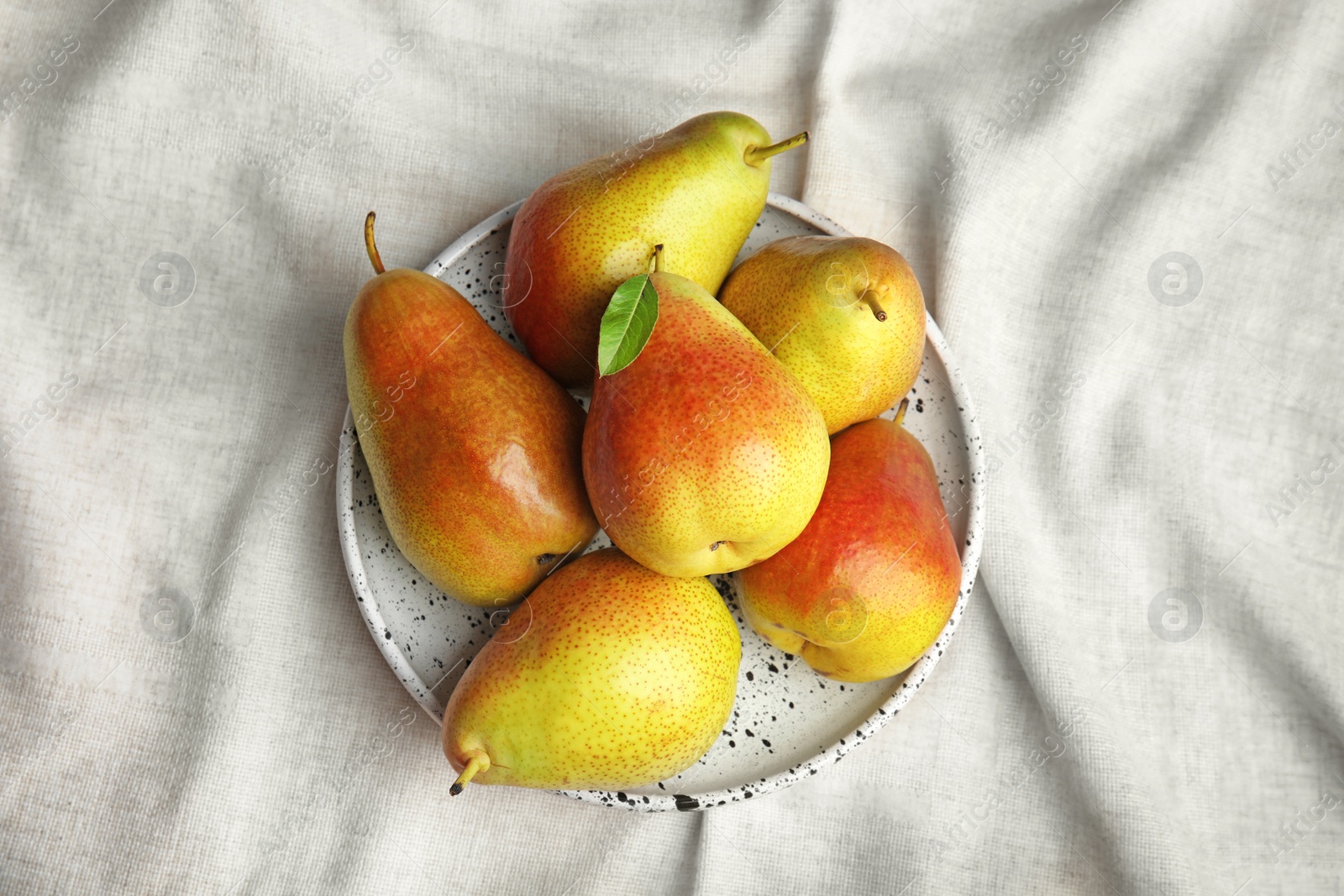 Photo of Plate with ripe juicy pears on light fabric, top view