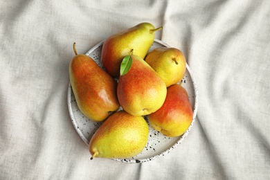 Plate with ripe juicy pears on light fabric, top view