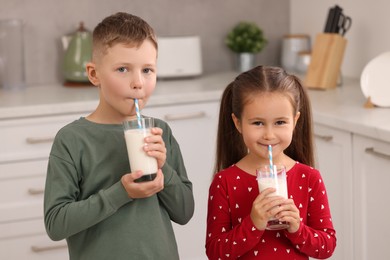 Cute children drinking fresh milk from glasses in kitchen