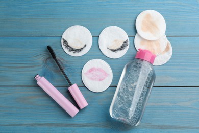 Dirty cotton pads, mascara and micellar cleansing water on blue wooden background, flat lay