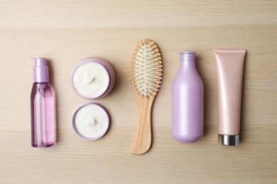 Different hair care products and brush on wooden table, flat lay