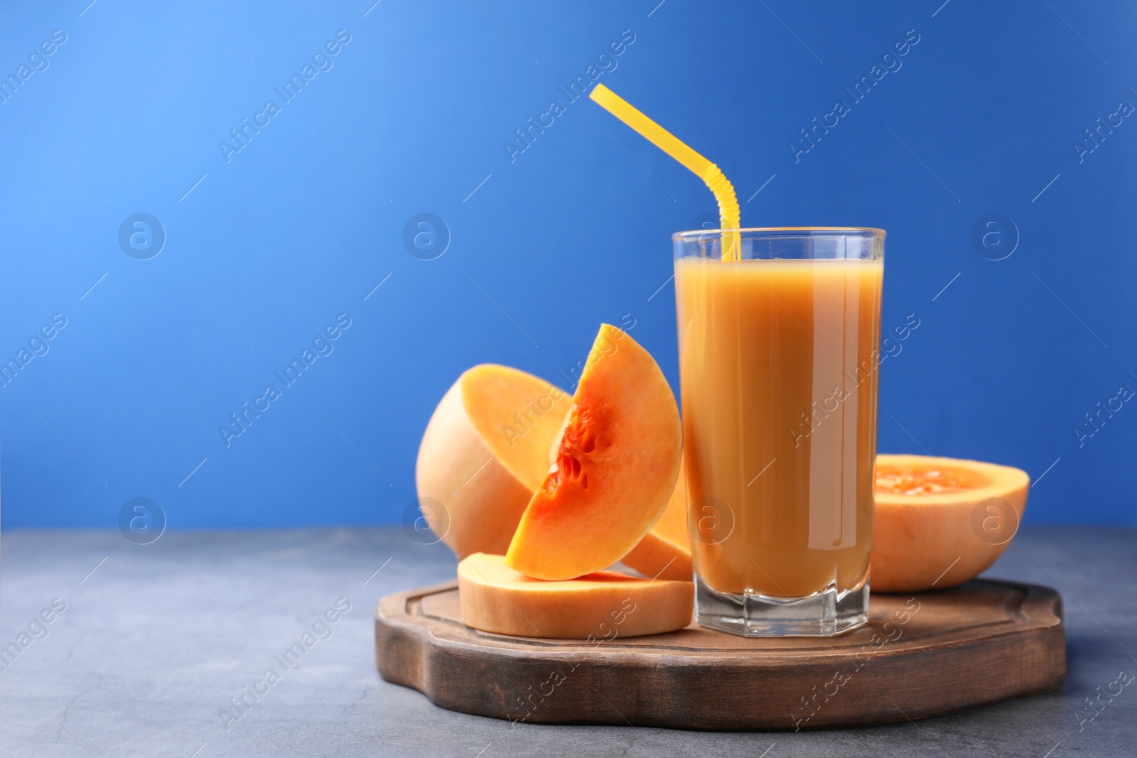 Photo of Tasty pumpkin juice in glass and cut pumpkin on light grey table against blue background. Space for text