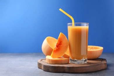Photo of Tasty pumpkin juice in glass and cut pumpkin on light grey table against blue background. Space for text