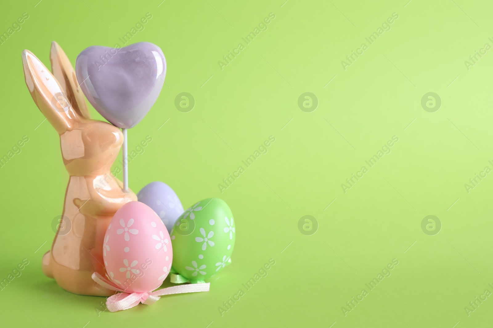 Photo of Easter bunny figure and dyed eggs on green background. Space for text