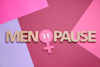 Photo of Word Menopause made of wooden letters and female gender sign on color background flat lay