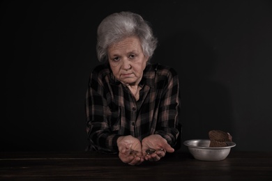 Poor mature woman with coins and bread in bowl at table