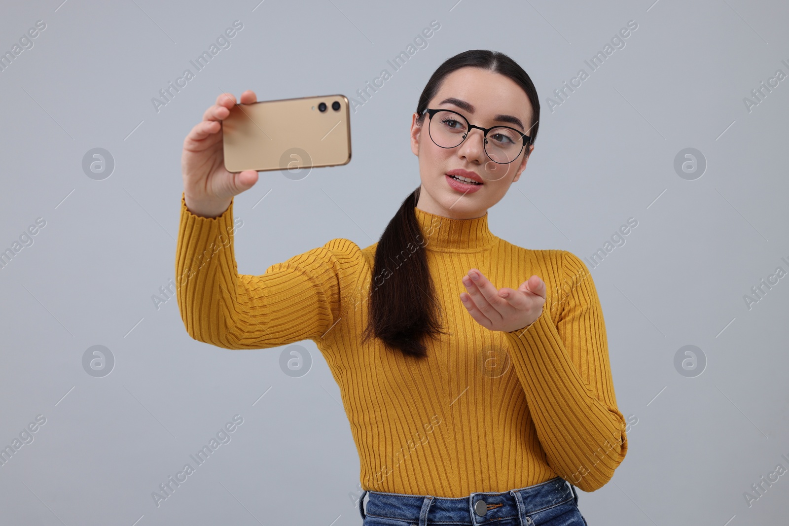 Photo of Young woman taking selfie with smartphone on grey background
