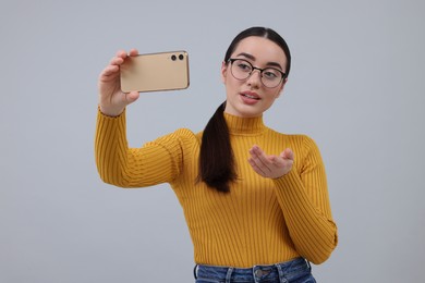 Young woman taking selfie with smartphone on grey background