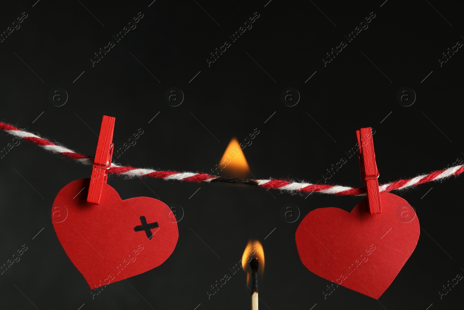 Photo of Red paper hearts on rope and burning match against black background. Composition symbolizing problems in relationship