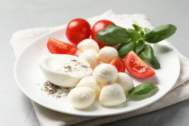 Photo of Delicious mozzarella with tomatoes and basil leaves on light gray table