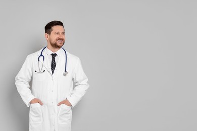 Portrait of smiling doctor on light grey background, space for text