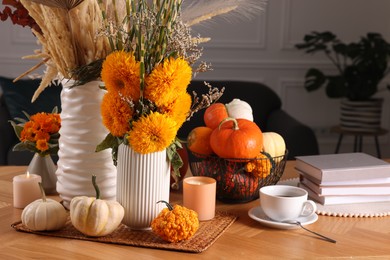 Beautiful autumn composition with bright orange flowers, pumpkins and burning candles on wooden table in room