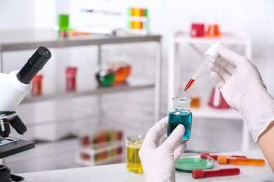 Photo of Scientist dripping reagent into bottle with sample in chemistry laboratory, closeup. Space for text