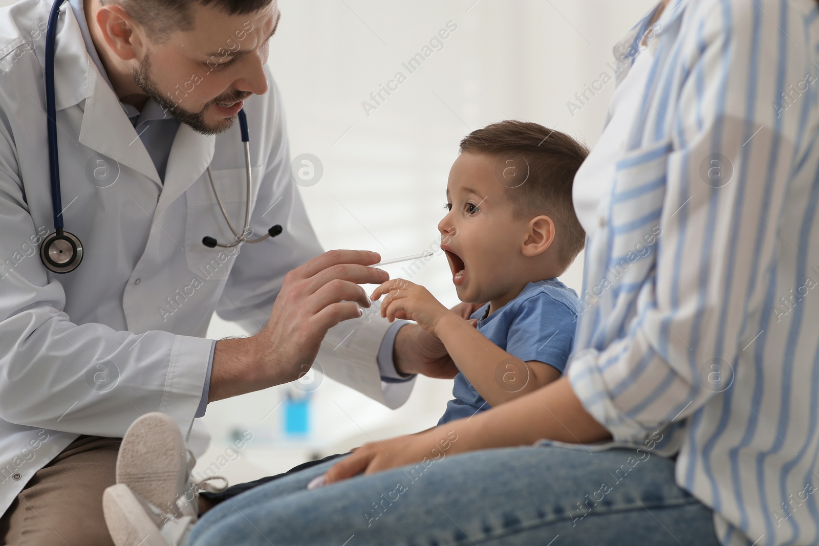 Photo of Mother and son visiting pediatrician in hospital. Doctor examining little boy