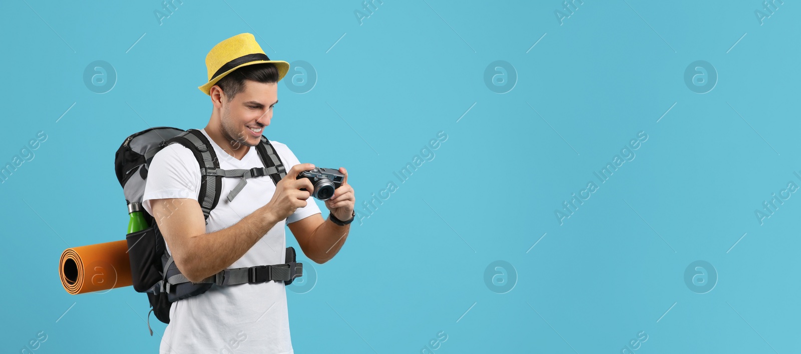 Photo of Male tourist with travel backpack and camera on turquoise background