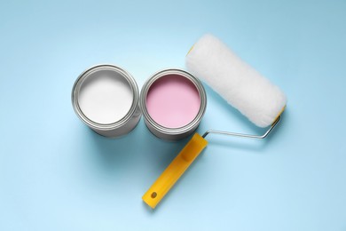 Photo of Cans with different paints and roller on light blue background, flat lay