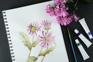 Photo of Flat lay composition with beautiful drawing of chrysanthemum flowers in sketchbook on black table